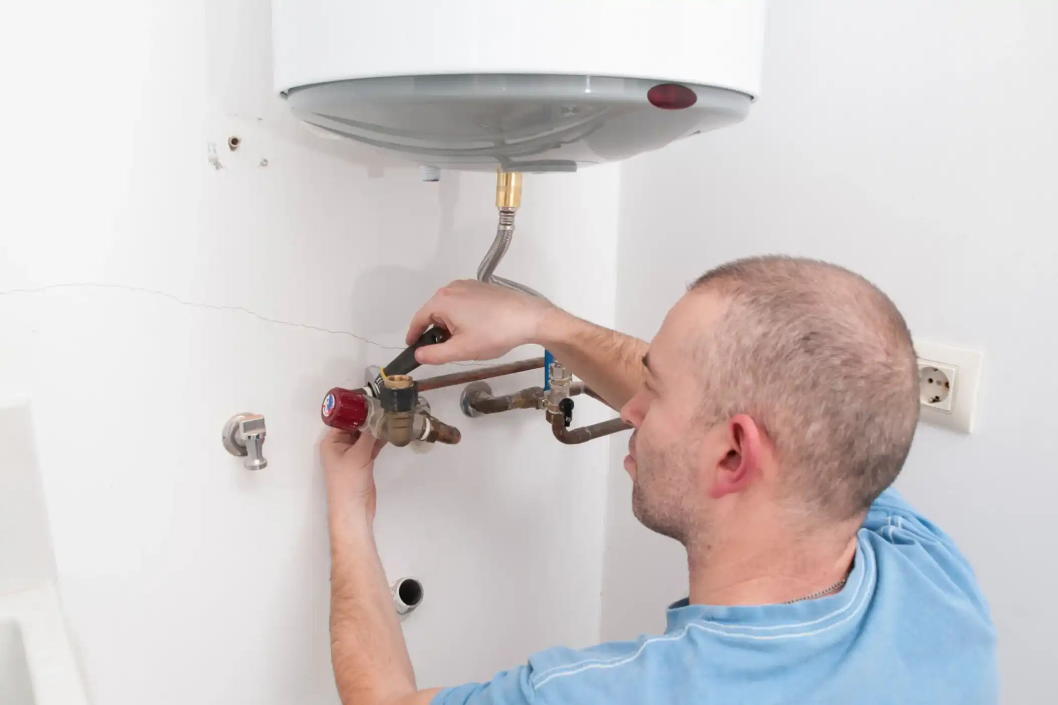 Close up view of young professional plumber in grey uniform holding wrench in hand on the kitchen